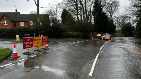 Supplied A street covered in water. Multiple roads signs are up marking a road closure and the diversion route. A police car can be seen in the background.