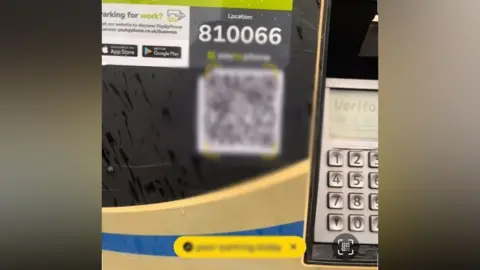 A closeup of a parking machine with a blurred out QR code.