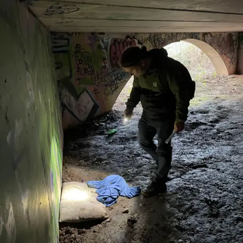 Richard shining is torch at a dirty pillow by the bridge wall 