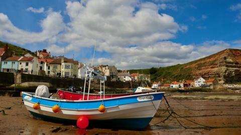 Small, beached boats in front of the picturesque coastal village of Staithes, below cotton wool clouds