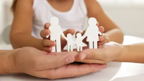 A stock image of adult and children's hands holding a white wooden cutout of a family