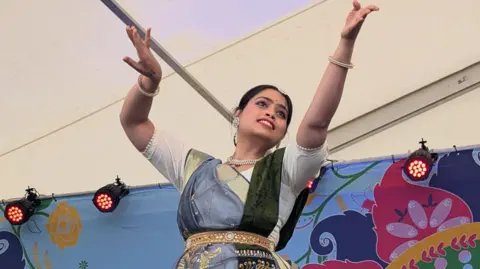A woman dances on stage in front of a colourful backdrop. 