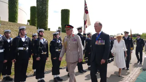 PA Media King Charles in a military outfit walking alongside another man past members of armed forces standing to attention.