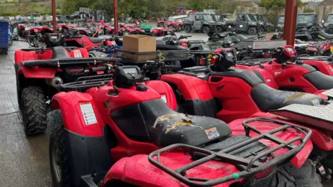 Lots of red quad bikes in the outside area of a farm