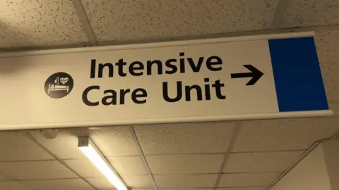 A achromatic  motion   suspended from a infirmary  corridor ceiling. "Intensive Care Unit" is written successful  ample  achromatic  letters, with a achromatic  arrow pointing to the right.