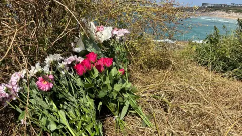 Pink and white flowers left on a cliff overlooking Fistral Beach in Cornwall.