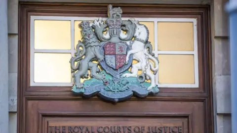 PA Media Crest above wooden door at The High Court in Belfast. There is a pane of glass behind the crest and on the wooden door are the words The Royal Courts of Justice.