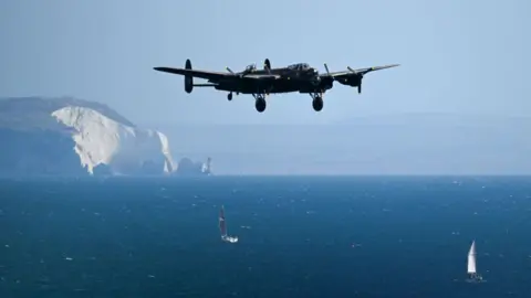 Getty Images A World War Two RAF Lancaster Bomber in flight over the sea, with the Isle of Wight in the background. Two sailing boats can be seen on the sea.