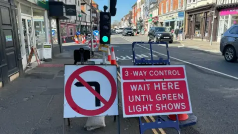 An image of the road works taking place in Farnham, Surrey. A 'three-way control' sign can be seen in the picture, as can a no left turn sign. A temporary traffic light is also visible. 