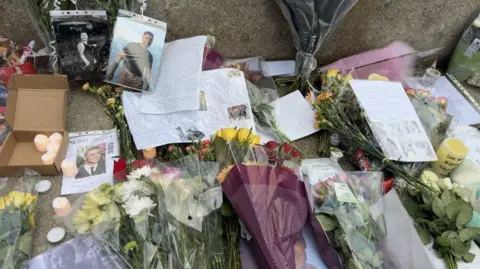 Bouquets of flowers, written tributes, candles and pictures of Liam Payne on a step