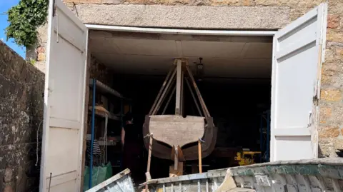 Historic, broken fishing boat with mould for new vessel in front