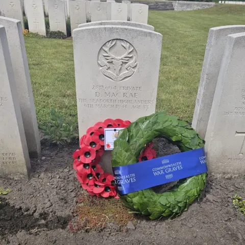 A gravestone with two wreaths laid against it