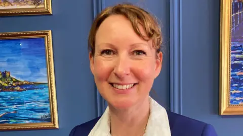 Dianne Matthews. She has tied back brown hair and is wearing a blue suit jacket and a white shirt.