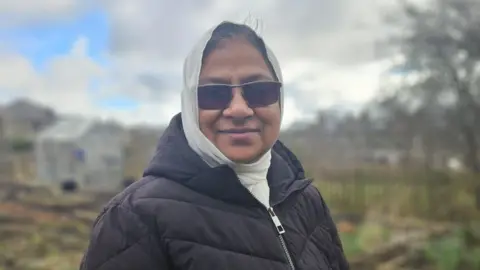 Aisha Iqbal/BBC A woman wearing a headscarf, black coat and dark-lensed glasses, pictured in an allotment.