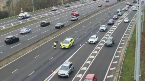 Traffic being siphoned off the M25. Road police are standing in the road and have laid out cones diverting traffic.