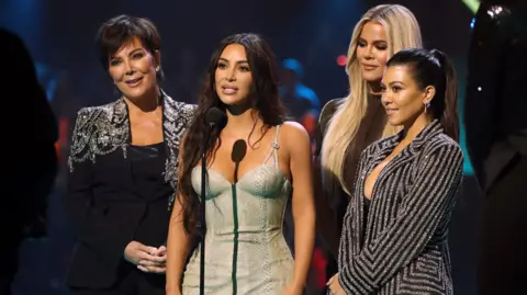 Getty Images Kris Jenner, Kim Kardashian, Khloé Kardashian, and Kourtney Kardashian onstage at an awards ceremony, dressed in glamourous outfits.