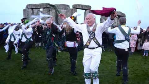 PA Media Morris dancers perform in front of Stonehenge as people take part in the winter solstice celebration