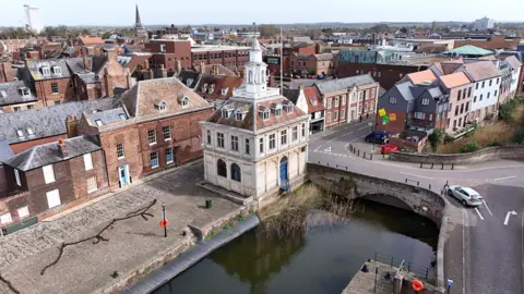 Samuel Garrod/KLWNBC Aerial view of King's Lynn Quayside showing brick wharf and the white stone Custom House on the waterside. Red brick properties can be seen in the distance and the spire of a church. 