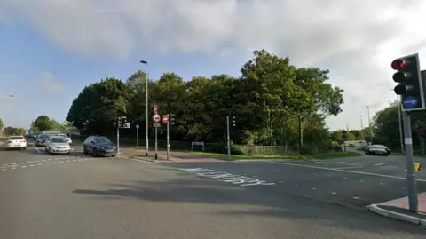 Street view image of the junction shows cars stopped at traffic lights. To the right of the cars are more traffic lights and a No Entry sign on the ground. 