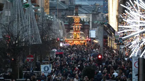 PA Media Shoppers throng Buchanan Street in Glasgow with Christmas lights and decorations visible in many of the shops