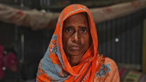 A woman wearing an orange saree looks into the camera 