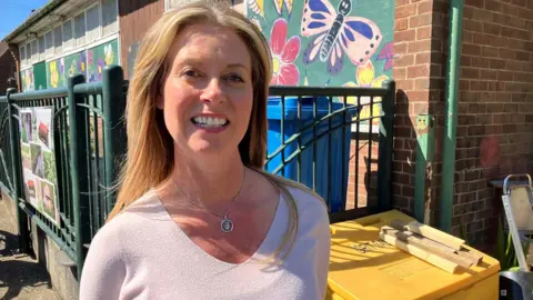A woman with long blonde hair is standing in front of a building with butterflies painted on the exterior walls.