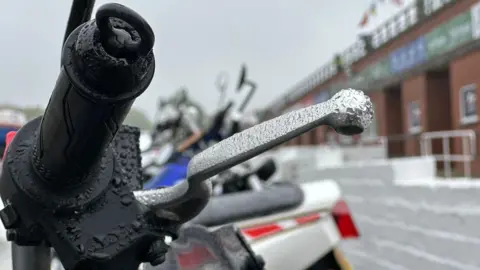 BBC Rain on the handlebars of a motorcycle parked at the grandstand.