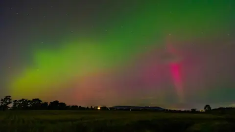 Ciaran Kelly/BBC News NI Weather Watcher The Northern Lights visible in the sky, which is blue, green and pink. 