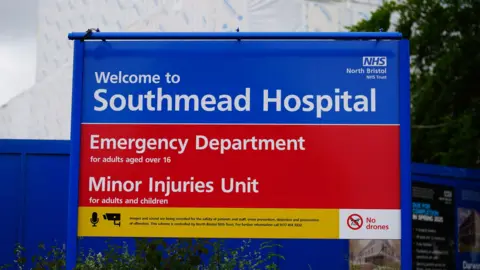 A sign outside Southmead Hospital. The sign is blue, with a red part showing directions to the Emergency Department and the Minor Injuries Unit.