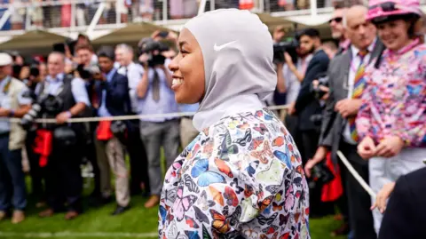 Goodwood Racecourse A female jockey wearing a hijab and top with colourful butterflies on it.