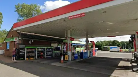 The front of Hedgeley Services petrol station. A person is withdrawing cash from the machine to the side of the brown brick one-storey building.