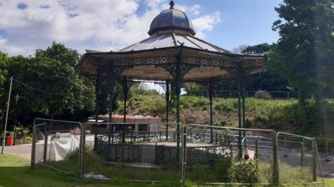 A bandstand surrounded by fencing in a park.