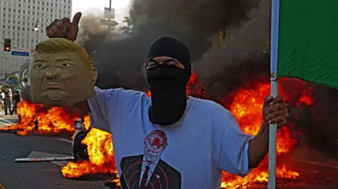 A protester holds a Mexican flag and mask of Donald Trump in LA on 8 June 2025 