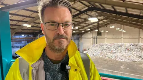 Councillor Watts in a hi viz jacket overlooking a mountain of plastic