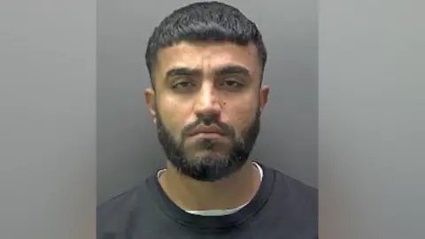 Hertfordshire Police A mugshot of Galmne, wearing a white t-shirt under a black sweater. He has a black beard and moustache and short dark hair.
Copyright
