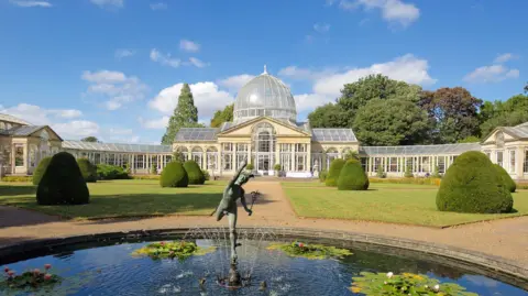 Neoclassical mansion with glass dome roof, and gardens with pond, as pictured in sunshine.