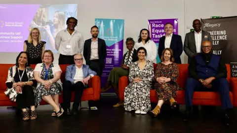 WMCA Members of the authority sitting on red sofas with some standing behind, the group totalling 13 people from a range of backgrounds and genders