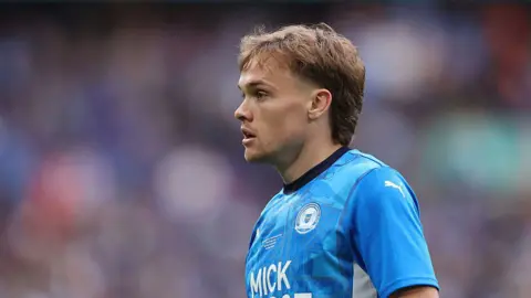 Getty Images Archie Collins looking to the left. He is wearing a blue Peterborough United top. The background behind him is blurred. 