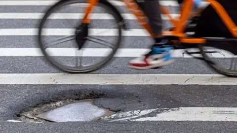 Getty Images The wheels of a bike can be seen, slightly blurred, passing close by a large pothole in a road.