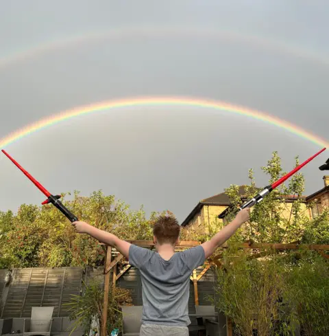 Alan Smith A boy holds two lightsabres at either end of a rainbow