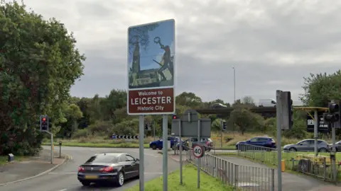 A sign saying "Welcome to Leicester - Historic City, next to a traffic island
