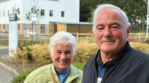 Sue and Gordon Pullin stand together outside the new care centre in Trowbridge. They both have short white hair. She is in a green jacket and he is in a darknavy or black one.
