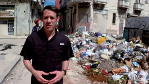 Will Gran in a black short sleeve shirt on a street in Havana covered in trash