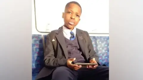 Daniel Anjorin wearing school uniform, sitting on a train
