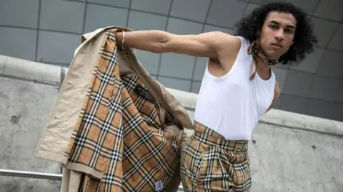 Getty Images A man takes off his Burberry trench coat to reveal matching Burberry check trousers