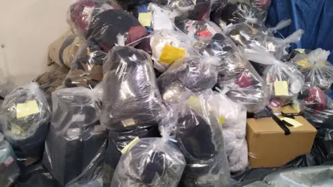 City of Wolverhampton Council More than a dozen clear plastic bags full of clothes are piled up against a wall