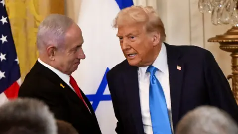 Donald Trump speaks to Benjamin Netanyahu as they shake hands in front of the US and Israeli flags at a press conference at the White House on 4 February