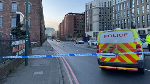 A police van and a cordon with blocks of flats on either side of a road 