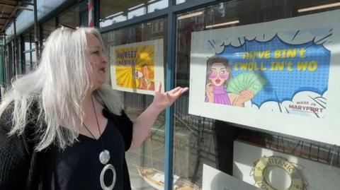 Woman outside pointing at sign with local dialect