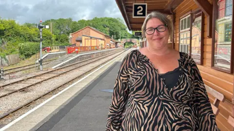 A woman is standing on a platform wearing a striped top. She is smiling.